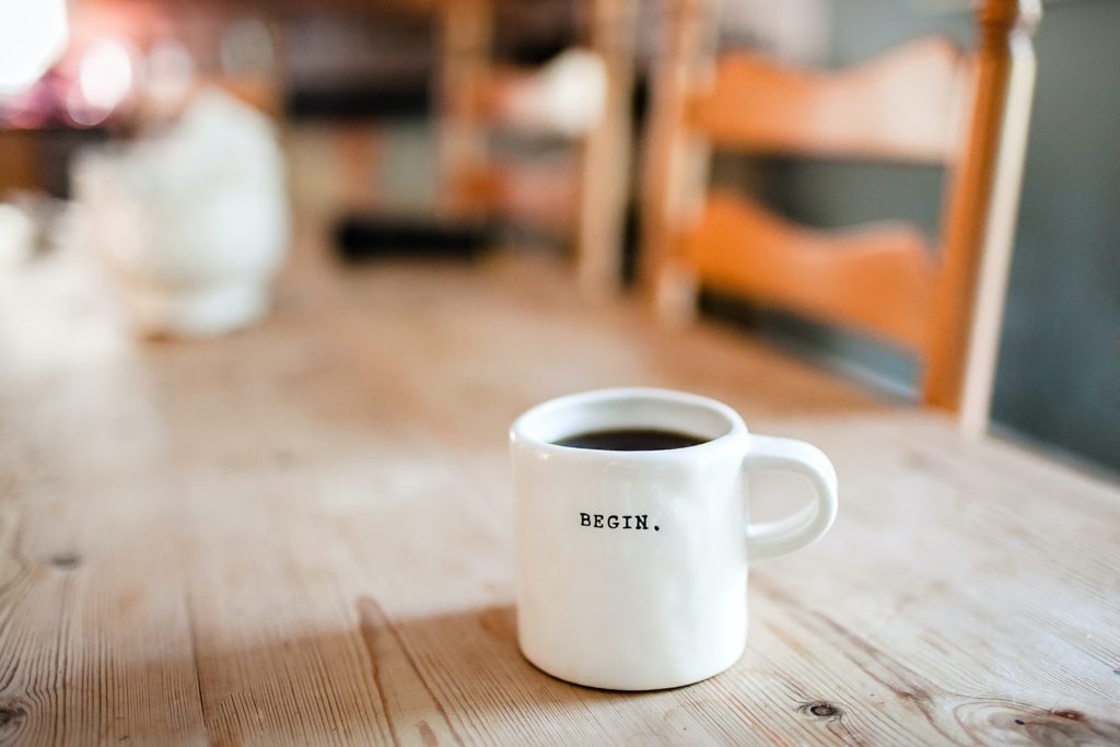Xícara de café sobre mesa de madeira com o dizer "begin", simbolizando o início do aprendizado das empresas tradicionais com as startups.